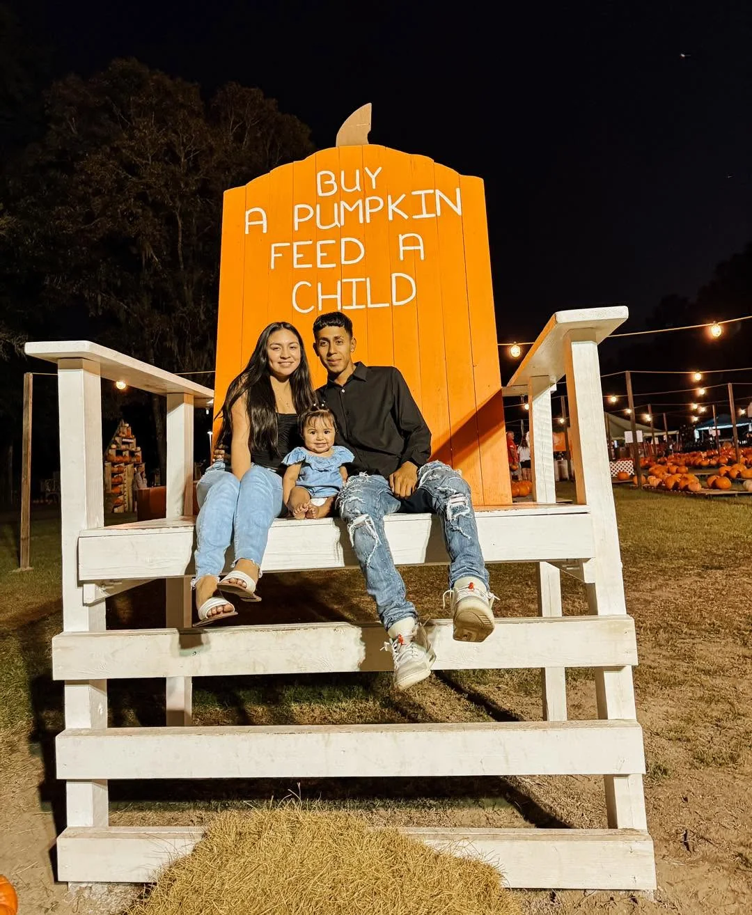 Family posing on the giant Buy A Pumpkin Feed A Child chair at night