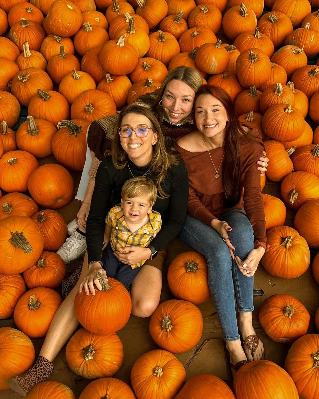 Family and friends smiling together among pumpkins at the patch